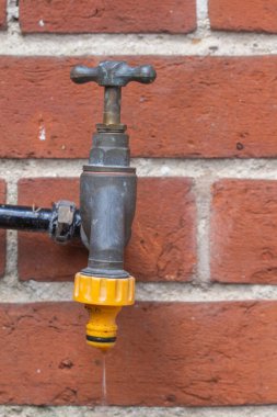 Tuğla duvara monte edilmiş, çalışan bir bahçe musluğunun yakın plan resmi