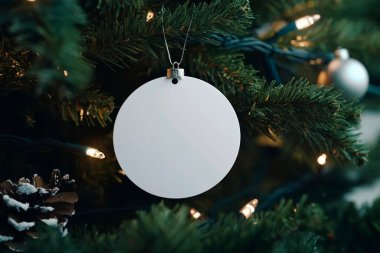 Blank ornament hanging on a Christmas tree surrounded by warm lights. clipart