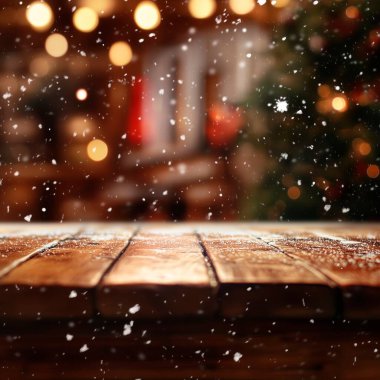 Snowfall on rustic wooden table with warm festive lights in the background. clipart