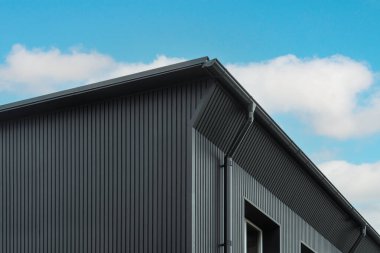 Modern architectural detail of a sleek gray building against a blue sky. clipart