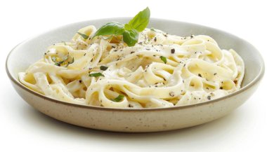 Taze fesleğen ve biberle süslenmiş lezzetli bir tabak fettuccine Alfredo..