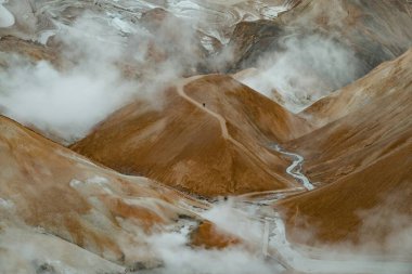 Aerial view of rugged mountains with a winding path in a misty landscape. clipart