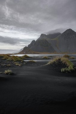 Dramatic landscape of dark volcanic sand and mountains under moody skies. clipart