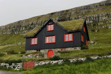 Traditional black wooden house with red accents set against a grassy hillside. clipart