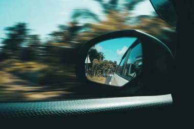 Side view of a car mirror reflecting a scenic road with lush greenery. clipart