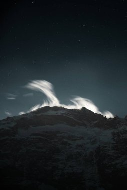 Majestic mountain peak under a starry night sky with ethereal clouds. clipart