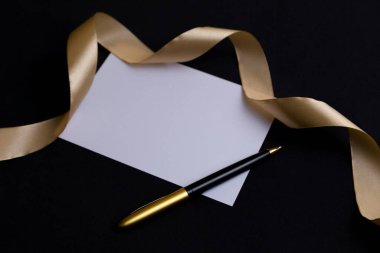 Elegant blank card with a gold ribbon and pen on a black background. clipart