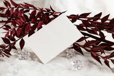 Blank card with red leaves and decorative crystals on a textured fabric background. clipart