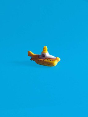 A bright yellow toy submarine against a vivid turquoise background. clipart