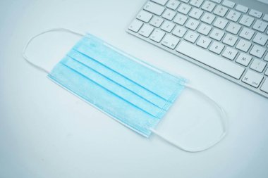 Blue surgical mask resting on a white keyboard. clipart