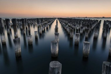 Serene sunset over calm waters with wooden pilings creating a captivating pattern. clipart