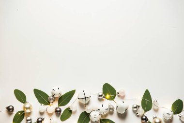 Elegant holiday decorations with white and gold bells and greenery on a neutral background. clipart