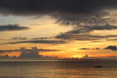 Silhouetted fishermen on a calm sea at sunset with dramatic clouds. clipart