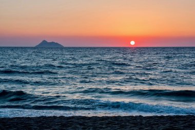 Sunset over the ocean with a distant island silhouette. clipart