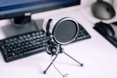 Close-up of a microphone with pop filter against a desktop computer setup. clipart