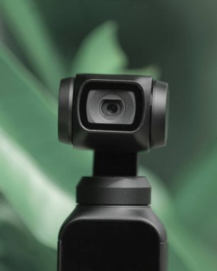 Close-up of a sleek black camera lens against green foliage. clipart