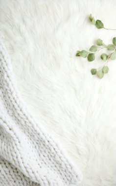 A cozy white knit blanket draped on a fluffy surface with green leaves for a serene ambiance. clipart