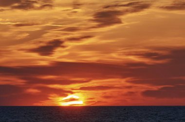 Stunning sunset over the ocean, painting the sky in vibrant orange and yellow hues. clipart