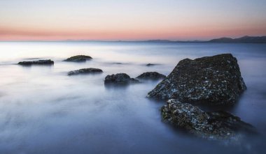 Serene seascape at dusk with smooth water and rugged rocks. clipart