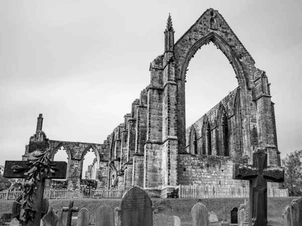 Bolton Abbey in black and white pictured in October 2022 behind headstones in Yorkshire.