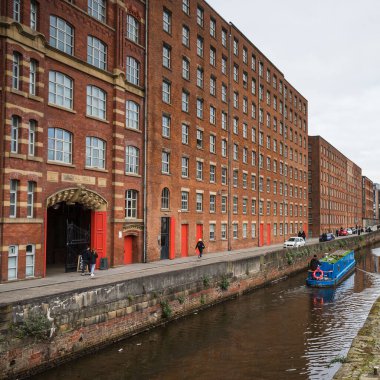 A blue narrow boat contrasts against the traditional red bricks of Royal Mill along Redhill Street in the Ancoats area of Manchester in February 2023.