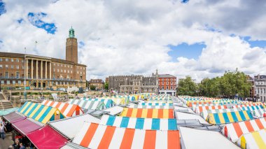 Norwich City Hall ve Norwich Guildhall tarafından çevrelenmiş Norwich pazarının çizgili çatılarının yer aldığı çok görüntülü bir panorama..