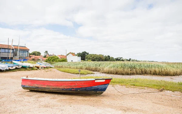 Kuzey Norfolk sahilindeki Brancaster Stadyumu 'nda halat ve çapasının arkasında kırmızı ve mavi ahşap bir tekne görülüyor..