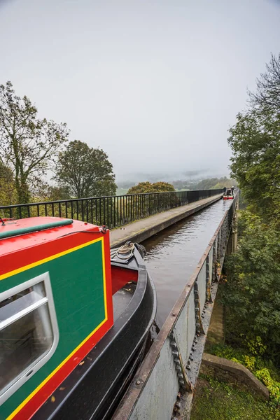 A colourful narrow boat travels along the Pontcysyllte Aqueduct towards the mist in the distance.