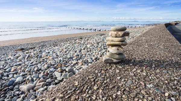 A rock stack seen on the promenade at Barmouth in Wales under a bright sky.
