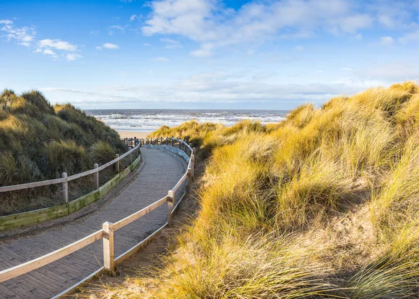 A multi image panorama of a curving board walk weaving through the sand dunes leading to the stunning beach and coast at Formby near Liverpool.