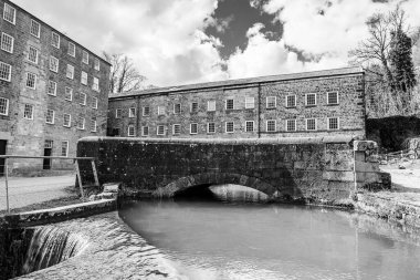 A black and white image of water flowing from Cromford Mill seen near Matlock in Derbyshire in March 2024. clipart