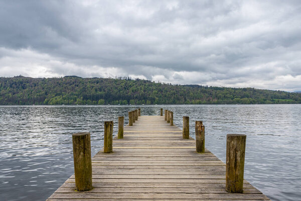 Looking down wooden jetty with tying posts jutting out into Lake Windermere in May 2024.