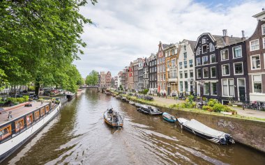 Hollanda 'nın Amsterdam kentindeki güzel Prinsengracht kanalında 26 Mayıs 2024' te resmedilen küçük bir tekne kasaba evlerinin yanından geçiyor..
