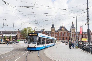 28 Mayıs 2024 'te, Hollanda, Amsterdam Centraal' ın dışında turist ve banliyö yollarında yürüyen turistlerin durduğu mavi ve beyaz bir tramvay görüntülendi..