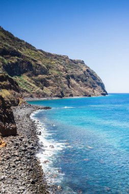 2024 yazında mavi gökyüzünün altında görülen Madeira Adası 'ndaki Porto Moniz' in sarp kıyılarına dalgalar çarpar..