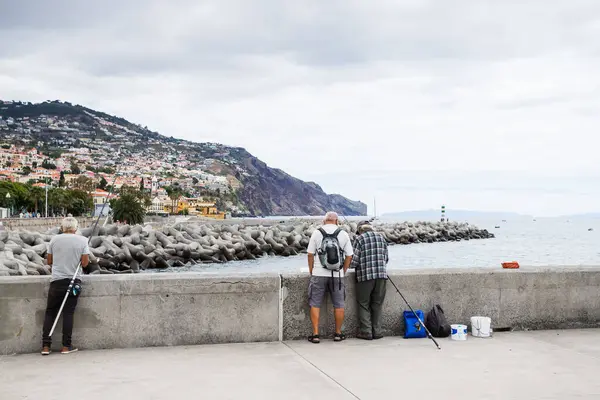 stock image Three men pictured by a wall on the promenade and waterfront of Funchal, Madeira fishing on the shores of the Atlantic Ocean on 31 July 2024.