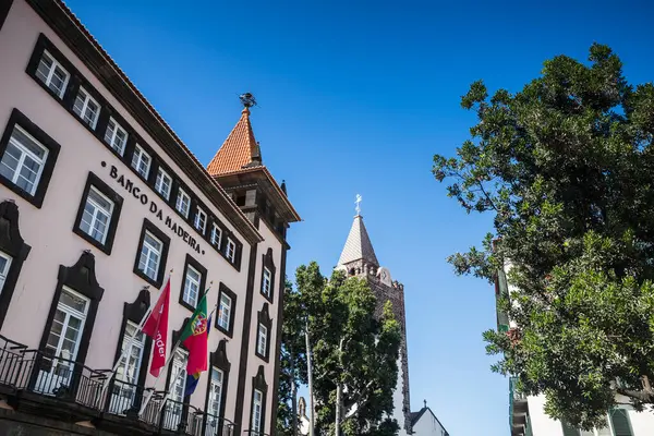 stock image Banco da Madeira (Bank of Madeira) pictured next to the bell tower of Funchal Cathedral seen in Madeira on 6 August 2024.