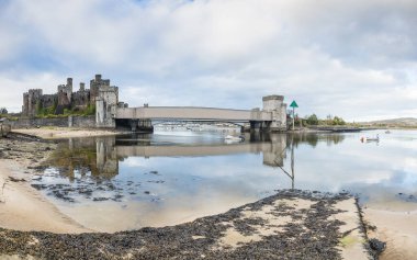 A multi image HDR panorama looking down a sandy slipway towards Conwy Castle and the Conwy Suspension Bridge pictured reflecting in the low tide on 26 October 2024 in North Wales. clipart