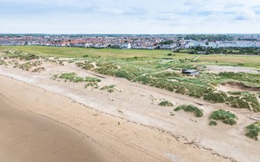 Liverpool yakınlarındaki Crosby plajındaki kum tepelerinin arkasında yalnız bir Demir Adam heykeline bakan bir hava görüntüsü..