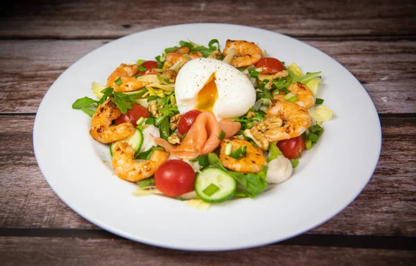 Recipe for rocket salad, endive, tomato, cucumber, soft-boiled egg, fried shrimp with paprika, smoked salmon and nuts. High quality photo