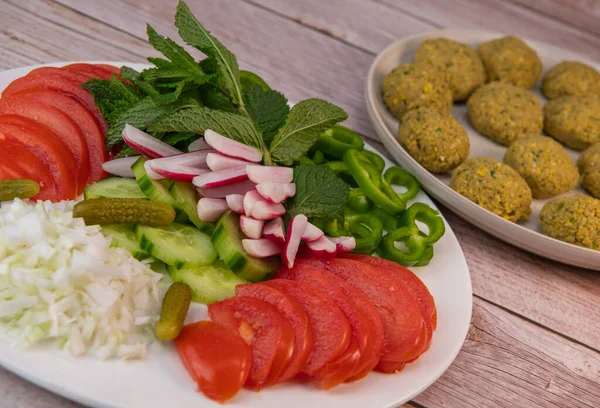 stock image Plate of fresh vegetable salad, tomato, cucumber, onion, gherkin, radish, mint leaves and falafel, High quality photo