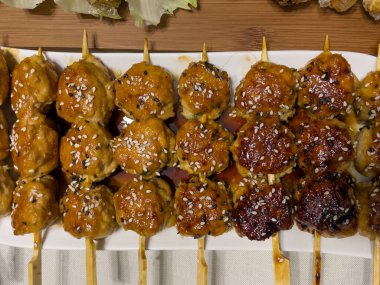Kızarmış et köfteleri beyaz bir tabakta bambu şiş, masada baharatlı sos, kaliteli fotoğraf.