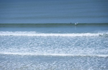 İki sörfçü, sakin bir günde Biscarrosse Sahili 'nde dalgalanan dalgalarda dolaşır. Sakin sular masmavi gökyüzünü yansıtıyor ve mükemmel bir sörf ortamı yaratıyor..