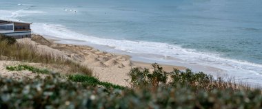 Dalgalar Biscarrosse 'un kumlu sahillerinde yavaşça dolaşırken arka planda yumuşak kum tepeleri yükseliyor ve sakin bir günde sakin bir sahil ortamı yaratıyor..