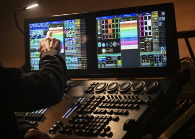 Yetenekli bir teknisyen dijital kontrol panelindeki ışıklandırma ayarlarını ayarlıyor ve popüler bir mekandaki canlı konserin heyecan verici atmosferine katkıda bulunuyor..