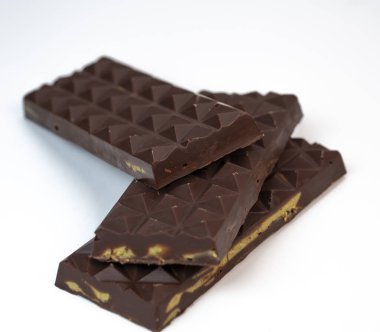 Yığınlanmış kadaif katmanları zengin bir çikolata tabakasını kucaklıyor ve üzerinde bir fıstıkla, leziz dokuları ve tatları bir mutfak sunumunda sergiliyor..