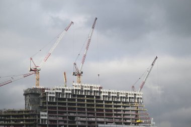 Turnalar Paris 'te bir inşaat sahasında faaliyet gösteriyor. İşçiler, bulutlu hava koşulları altında modern bir gökdelen inşaatının geliştirilmesinde aktif rol alıyorlar..