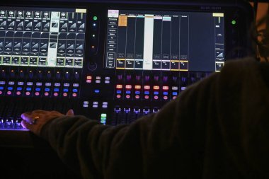 Odaklanmış ses mühendisi, canlı bir mekan atmosferindeki performansa hazırlanırken sürgüleri ve düğmeleri dijital karıştırma konsoluna ayarlar.