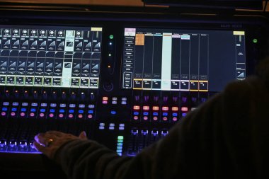Fransa, Nisan 2025: Odaklanmış ses mühendisi, canlı bir mekan atmosferindeki performansa hazırlanırken sürgüleri ve düğmeleri dijital karıştırma konsoluna ayarlıyor.