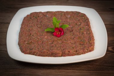 Kebbe naye, zengin bir mutfak deneyimi için tasarlanmış bulgur, soğan, nane ve baharatla karıştırılmış ince doğranmış çiğ et içeren beyaz bir tabakta sergileniyor..